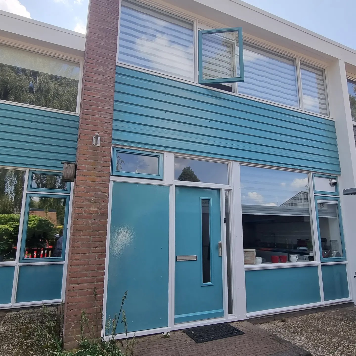 Voorgevel met petrolblauwe gevelbekleding, voordeur en wit geschilderde kozijnen