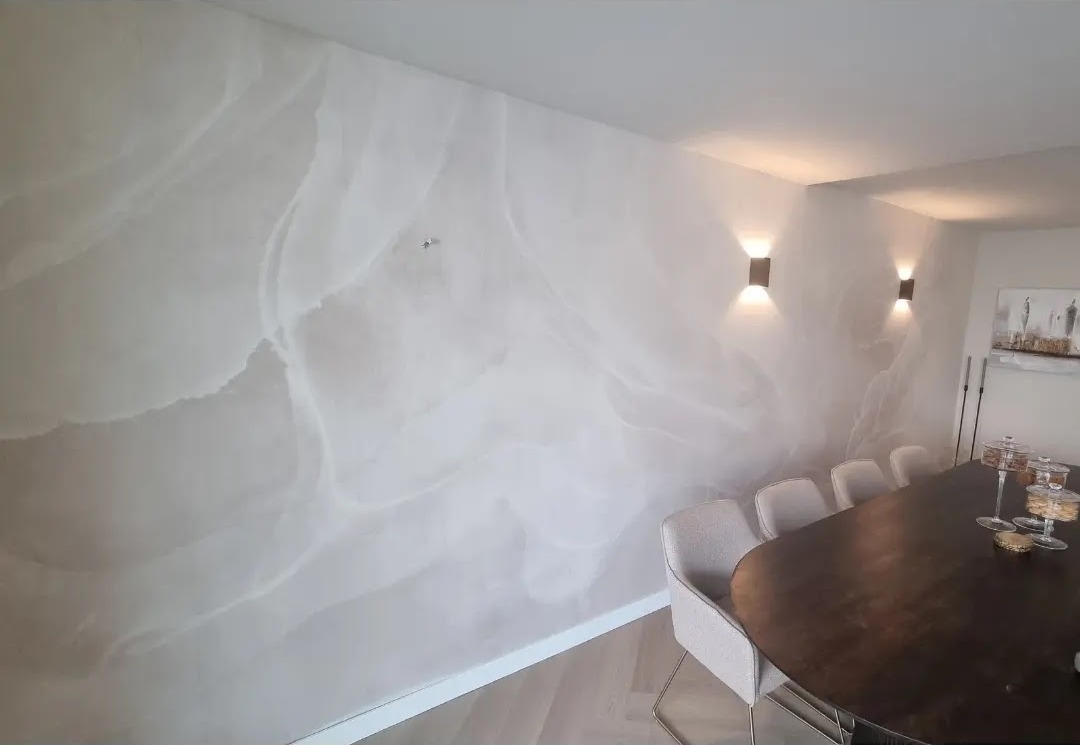Eetkamer met een wand in lichte marmerlook en wandlampen