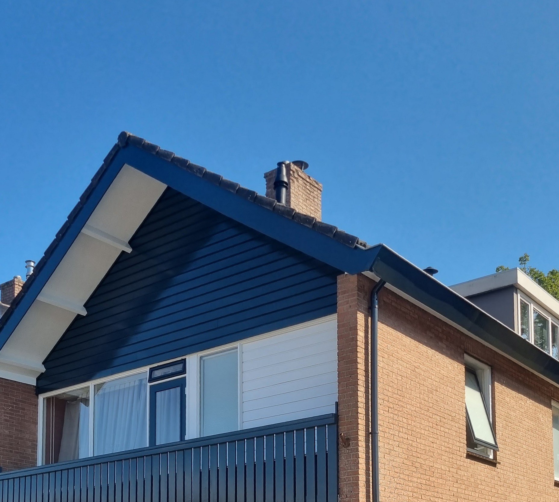 Woning met donkerblauw geschilderde topgevel, balkon en witte kozijnen