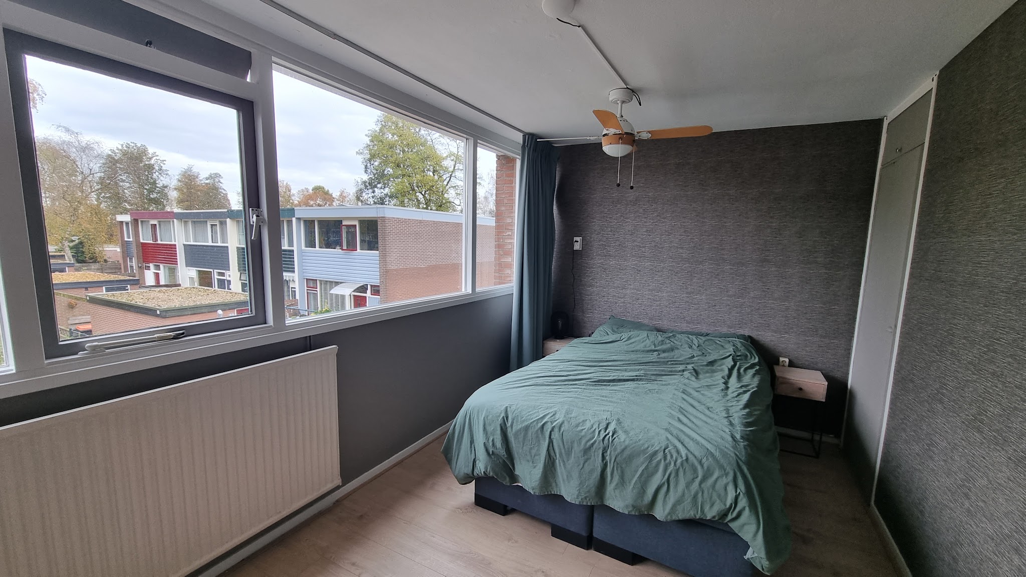 Slaapkamer met grijze wandbekleding, groot raam en opgemaakt bed
